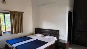 A hotel room with a bed, a nightstand, a wardrobe, and a window with curtains. - Eagle Eye Resort (Mahabaleshwar)