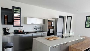 Et moderne køkken med stålemfang, en central ø og et spiseområde med et træbord og stole.