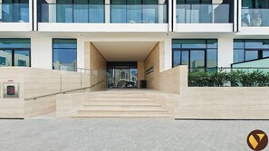 A modern building entrance with a glass facade, a staircase leading to the entrance, and a small outdoor area with plants. - Vogue | Binghatti Galaxy JVC near Circle Mall (Dubai)