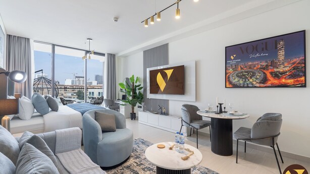 A modern hotel room with a sofa, armchairs, a round coffee table, and a city view. - Vogue | Binghatti Galaxy JVC near Circle Mall (Dubai)