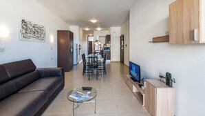 A modern living room with a sofa, a glass coffee table, and a flat-screen TV. - Seashells Apartment with Sea View Terrace (Bugibba,)