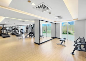 A modern gym with cardio machines, free weights, and a mirrored wall. - Bloomfields Studio in Julphar Residence-Reem (Abu Dhabi)