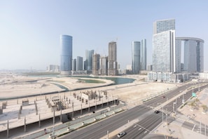 Un paysage urbain avec des gratte-ciel modernes, une promenade au bord de l’eau et une route où circulent des véhicules.