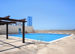 A rooftop pool with clear blue water, a pergola, and a city skyline in the background. - Bloomfields Studio in Julphar Residence-Reem (Abu Dhabi)