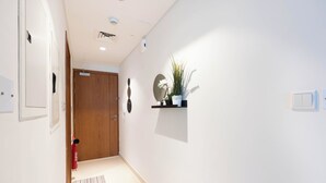 A hallway with a wooden door, a small shelf with a plant, and a fire extinguisher. - Bloomfields Premium STU Canal View (Abu Dhabi)