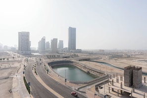 Un paysage urbain avec de hauts immeubles modernes, une vaste étendue d’eau et une large route où circulent des véhicules.