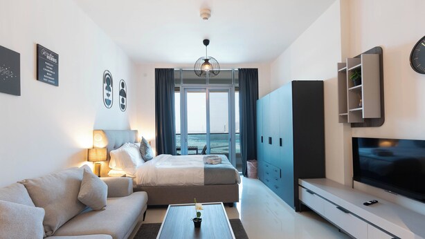 A modern hotel room with a bed, sofa, TV, and a view of the city. - Bloomfields Premium STU Canal View (Abu Dhabi)