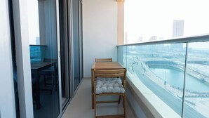 A balcony with a wooden table and chairs, a cushioned bench, and a view of a cityscape and water body. - Bloomfields Premium STU Canal View (Abu Dhabi)