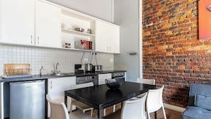 A compact kitchen with white cabinets, a black countertop, and a brick wall. - Long Street Self Catering Apartments (Cape Town)