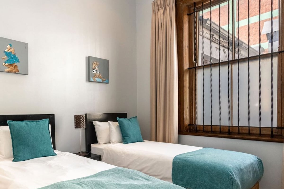A hotel room with two beds, a window with bars, and artwork on the wall.