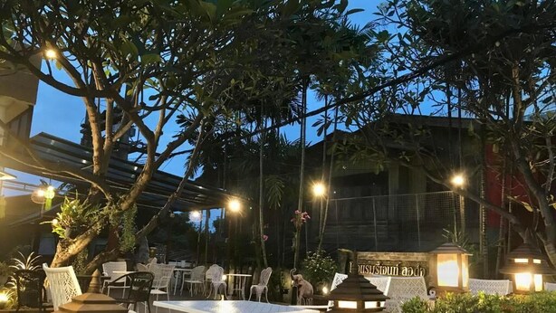 Un espacio de comedor al aire libre con mesas y sillas, rodeado de árboles e iluminado por faroles.