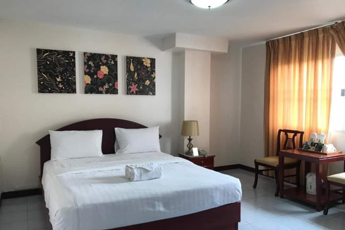 A hotel room with a large bed, a desk with a lamp, and two paintings on the wall.