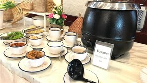 Una mesa de buffet con diversos platos y una olla grande con la etiqueta 'Porridge con pescado'.