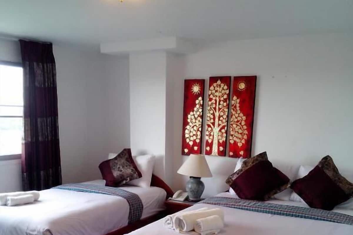 A hotel room with two beds, a bedside table with a lamp, and a wall-mounted artwork.