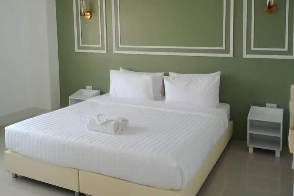 A neatly made bed with white linens and a rolled towel in a modern bedroom with green walls and white trim.