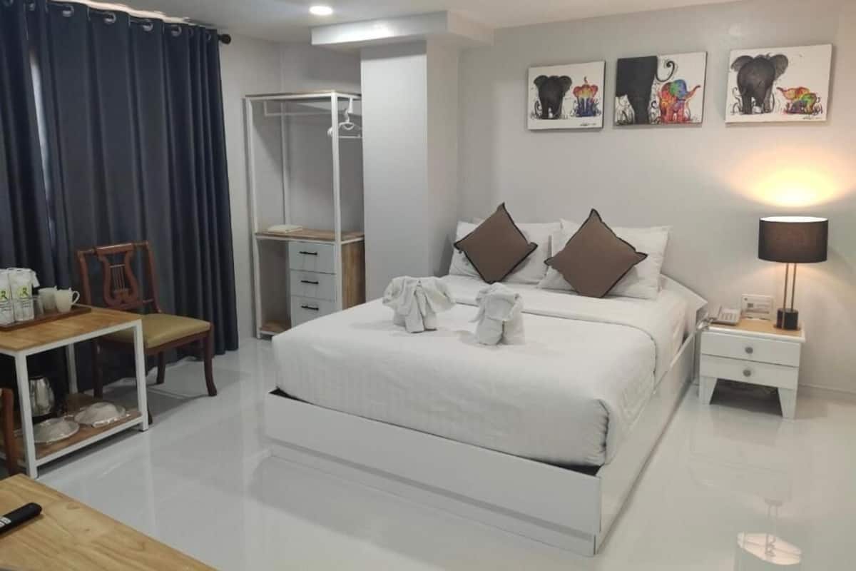 A hotel room with a large bed, a bedside table with a lamp, a wardrobe, and a small table with a chair.