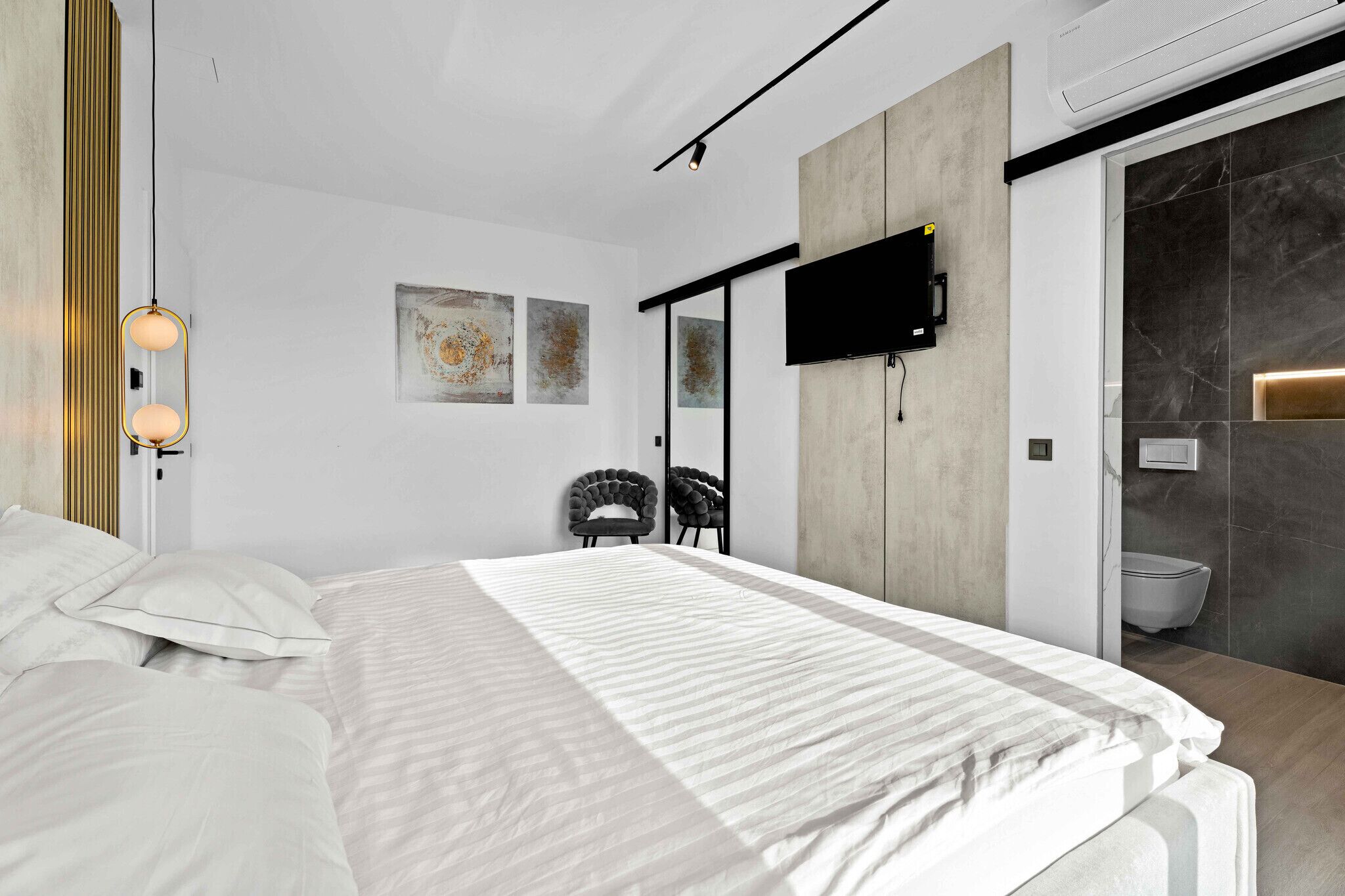Een moderne slaapkamer met een groot bed, een flatscreen televisie aan de muur en een schuifdeur naar een badkamer.