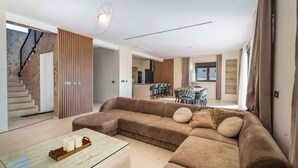 A modern living room with a large sectional sofa, a glass coffee table, and a staircase leading to an upper floor.