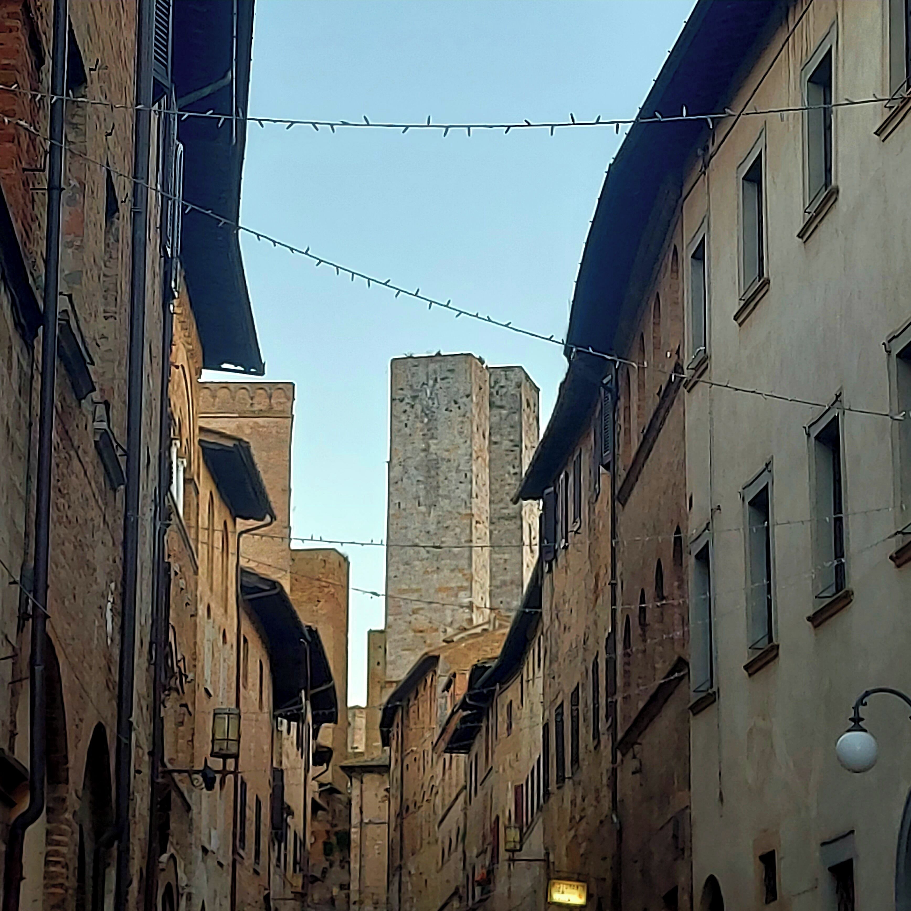 A narrow street with buildings on either side, featuring arched windows and a mix of brick and stone facades.