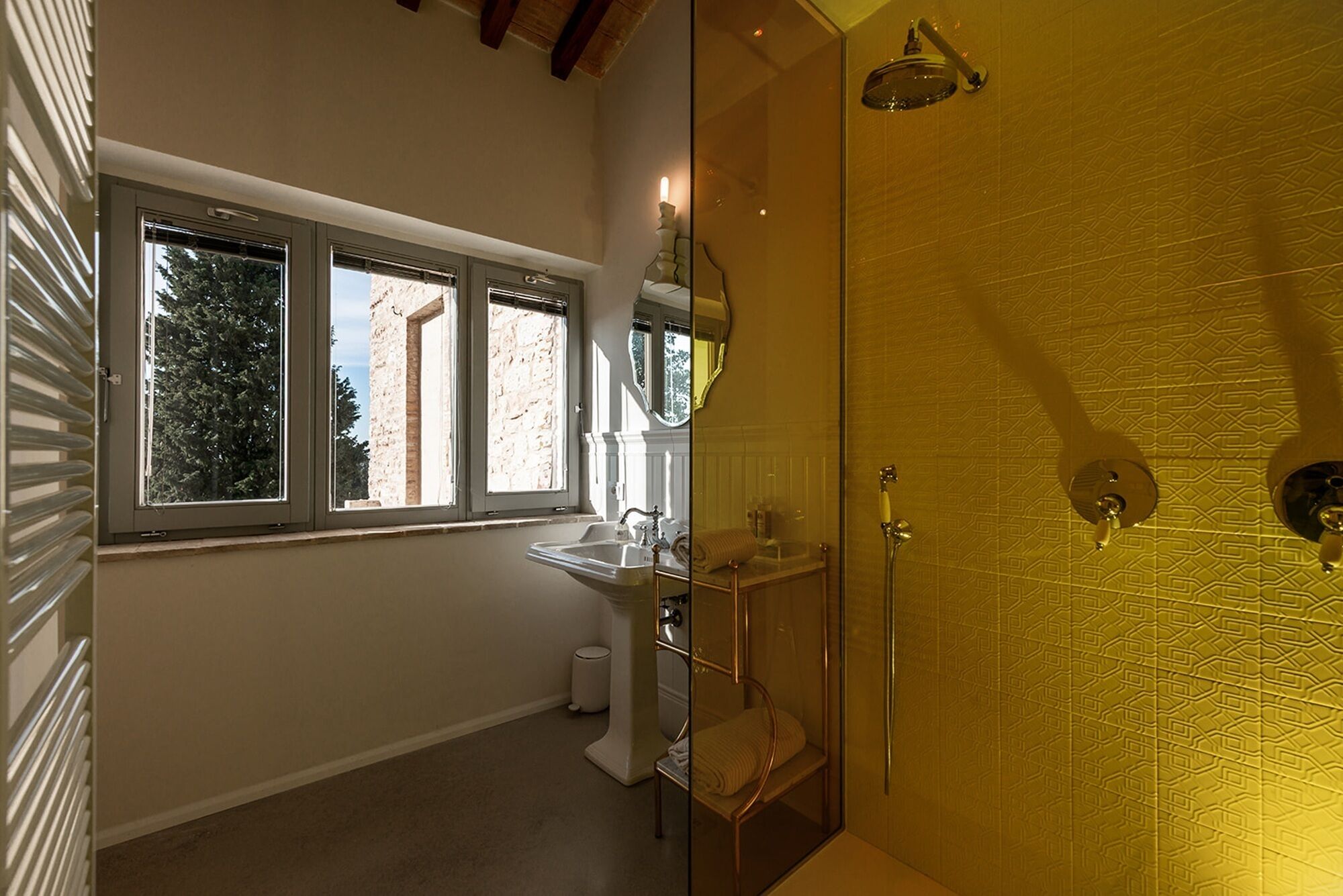 A bathroom with a sink, mirror, and shower. There are windows with views of trees and buildings.