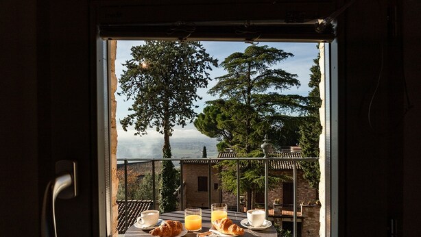 A breakfast setup with croissants, orange juice, and coffee on a balcony overlooking a scenic view with trees and a distant landscape. - Palazzo Sbaraglini (Assisi)