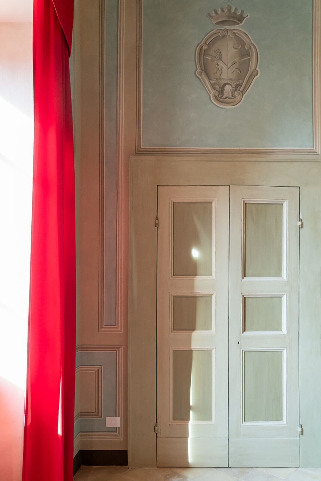 A room with a double door, a red curtain, and a decorative emblem on the wall.