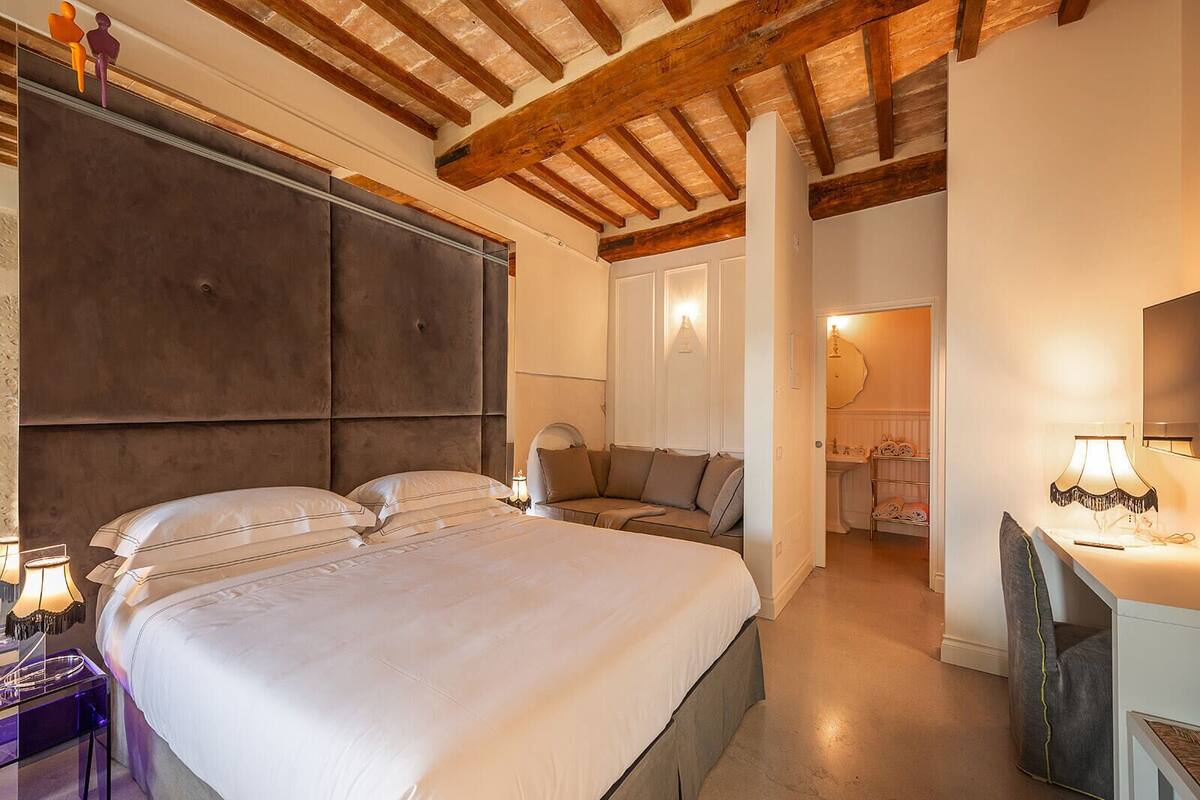 A bedroom with a large bed, a sofa, a desk, and a mirror.