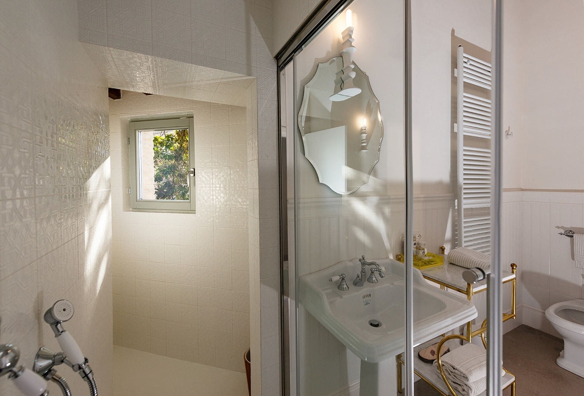 A bathroom with a glass-enclosed shower, a white sink with gold fixtures, and a toilet with a towel rack.