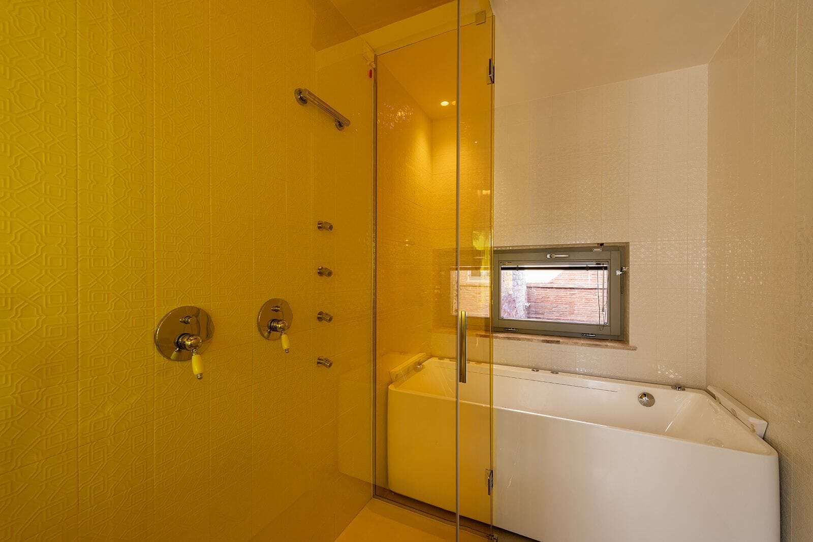 A bathroom with a glass shower enclosure, a bathtub, and a window.