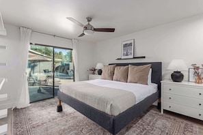 Un dormitorio moderno con una cama grande, un ventilador de techo, una mesita de noche con lámpara y vistas a un patio exterior.