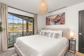 Ein Schlafzimmer mit einem großen Bett, Blick durch eine Schiebetür, einem Gemälde von Klippen und einer Nachttischlampe.