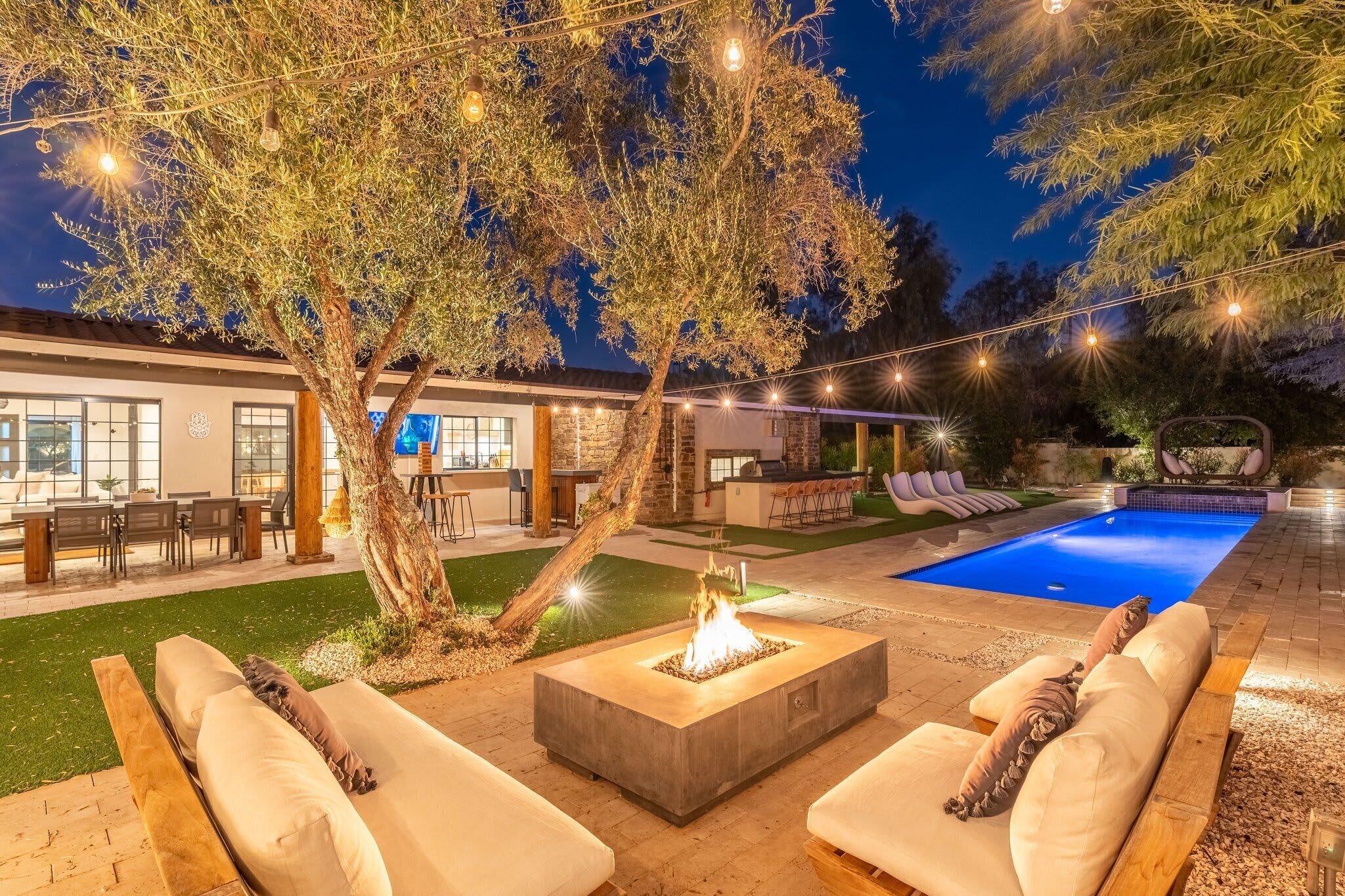 An outdoor pool area with a fire pit, lounge chairs, and string lights.