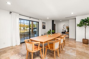 Ein Essbereich mit Holztisch und Stühlen, einem großen Fenster mit Vorhängen und einer Topfpflanze.