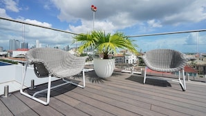 A balcony with two wicker chairs, a potted plant, and a city view.