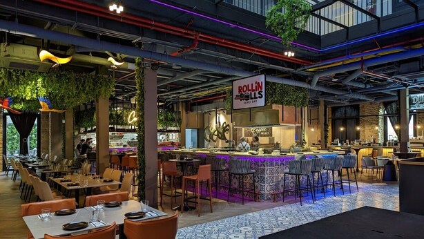 A modern restaurant with a bar area, indoor plants, and a mix of seating arrangements.