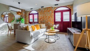 A modern living room with a sofa, coffee table, and TV stand. There are two arched doors and a ceiling fan.