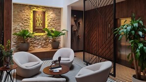 A modern lobby with a stone wall, two potted plants, and a seating area with two armchairs and a coffee table.
