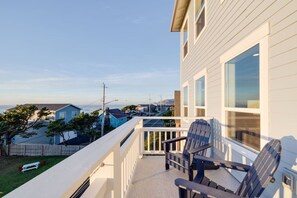 Een balkon met twee Adirondack-stoelen, een witte balustrade en uitzicht op omliggende huizen en de oceaan.
