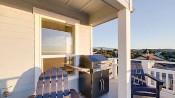 A covered outdoor area with a grill, Adirondack chairs, and a view of a residential neighborhood.