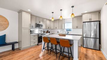 A modern kitchen with white cabinets, a stainless steel refrigerator, a central island with bar stools, and pendant lighting.