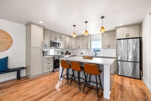 Een moderne keuken met witte kasten, een roestvrijstalen koelkast, een centraal kookeiland met barstoelen en hanglampen.
