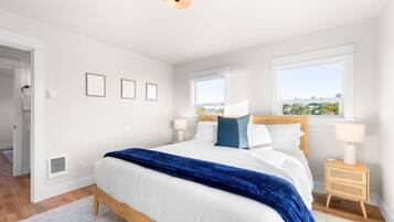 A bedroom with a large bed, two bedside tables, and a view of the outdoors through two windows.
