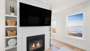 Una sala de estar moderna con chimenea, un televisor de pantalla plana montado encima y un ventanal con vistas al océano.
