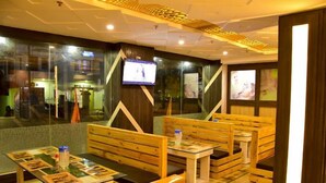 Ein Restaurant mit Holzbänken und -tischen, einem an der Wand befestigten Fernseher und Blick auf die Außenwelt durch große Fenster.