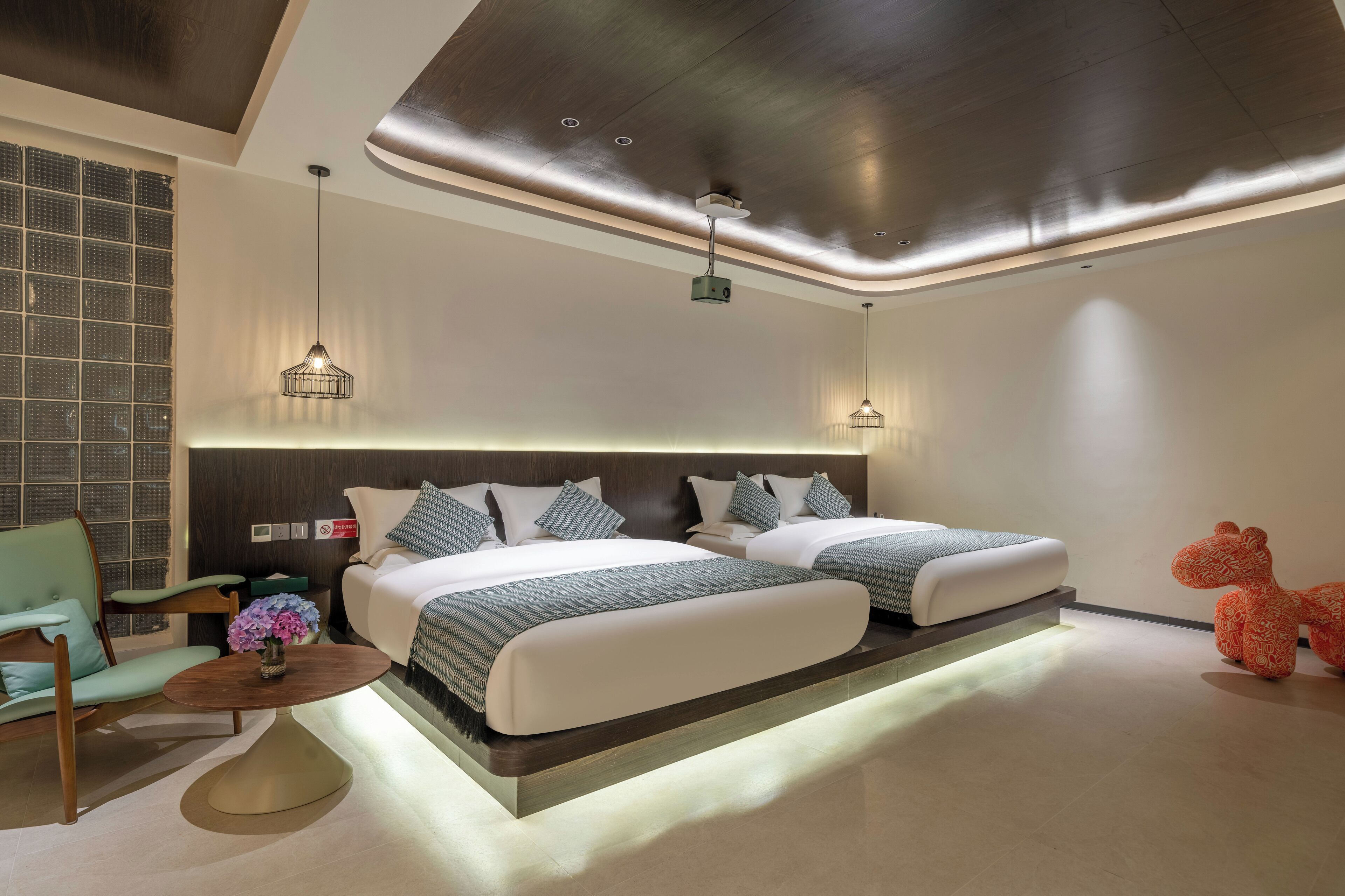 A modern hotel room with a large bed, a small table with a vase of flowers, a chair, and a decorative animal.