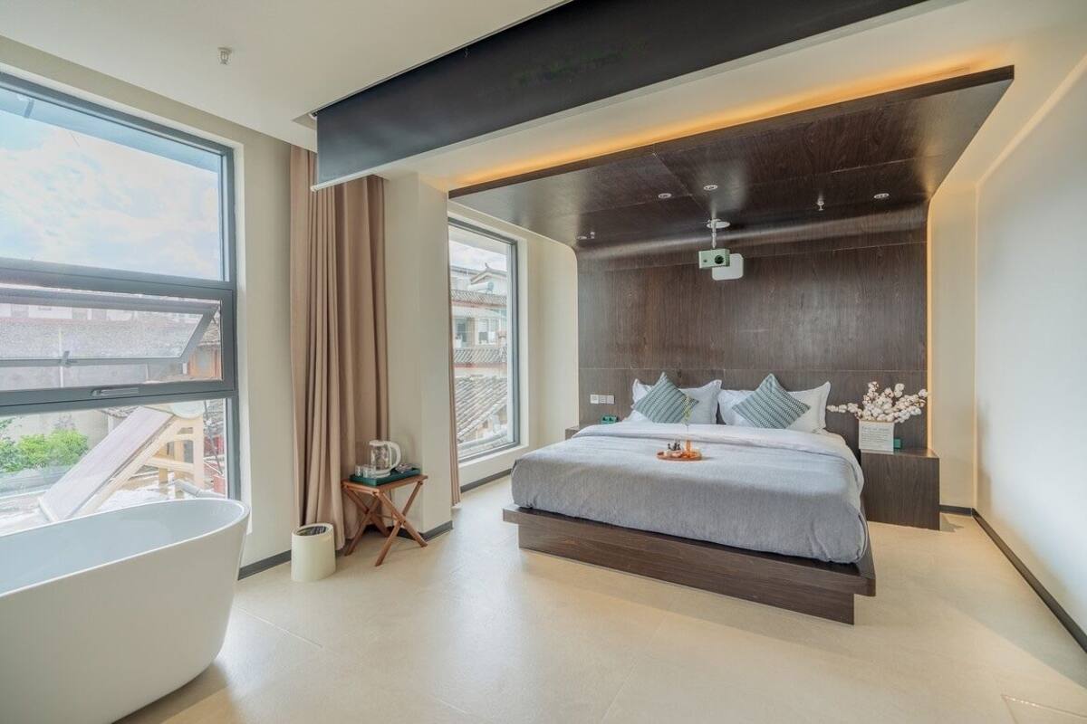A modern bedroom with a large bed, a bathtub, and a view of the city.