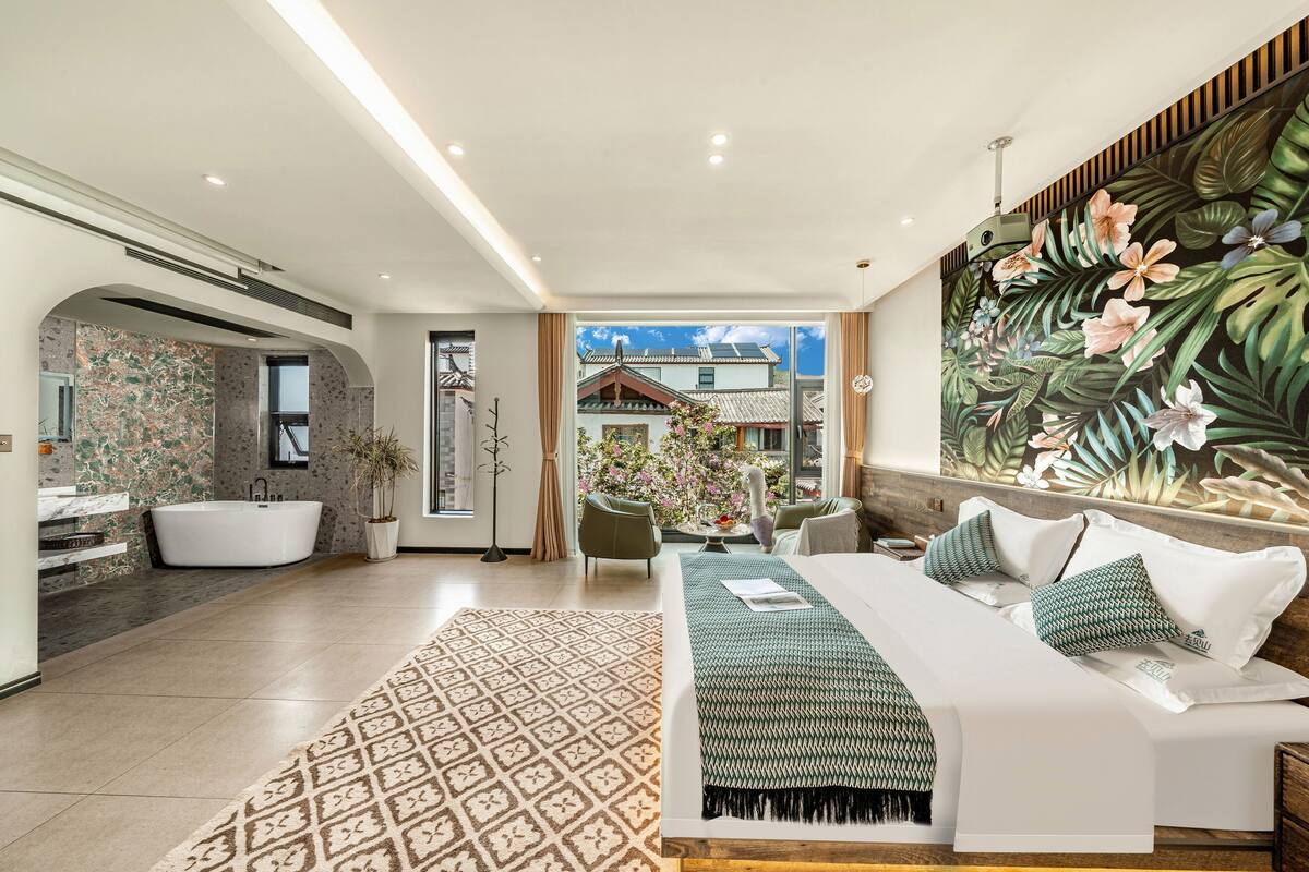 A modern hotel room with a large bed, a sitting area, a bathroom with a bathtub, and a view of a traditional building.