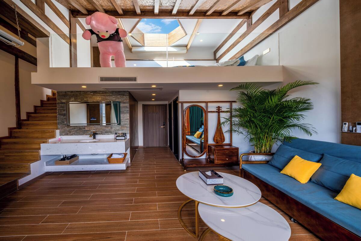 A modern living room with a staircase, a blue sofa, a coffee table, and a large potted plant.