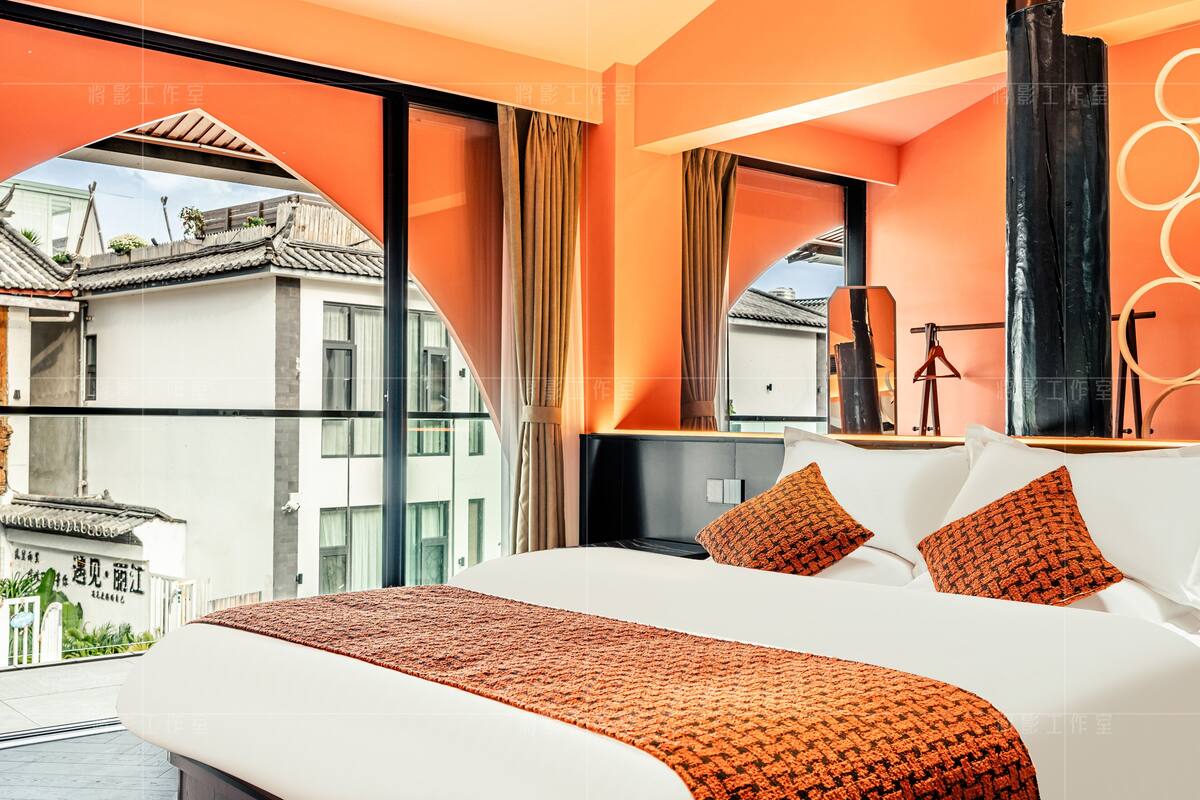 A modern hotel room with a large bed, orange bedding, and a view of traditional buildings outside.