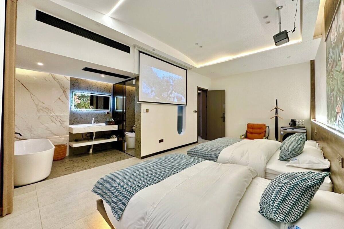 A modern hotel room with a large bed, a separate seating area with a TV, and a bathroom with a bathtub.